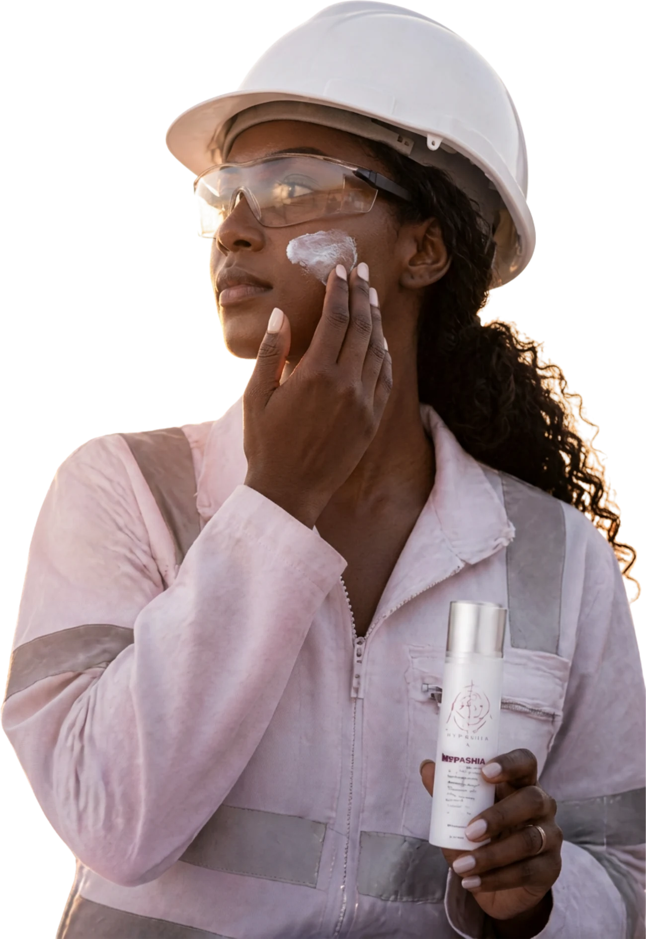 A site engineer in a white hard hat and safety glasses smoothing Hypashia lotion onto her cheek at sunrise